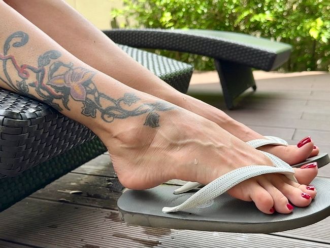 Neue Flip-Flops an meinen hübschen Füßen mit langen Zehen im Freien, rot lackierte Fußnägel