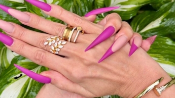 Neue lila Farbe Lange Nägel, scharfe Stilettos, Handflächen, lange Finger im Garten mit Blumen
