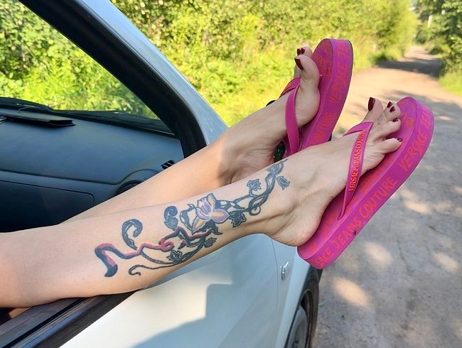 Rosa Flip-Flops an meinen hübschen Füßen mit langen Zehen im Freien, auf der Straße, im Gras, im Auto, rot lackierte Zehennägel