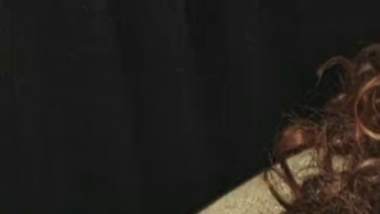 Sie sitzt in einem roten Morgenmantel und schwarzem BH, raucht und neckt.